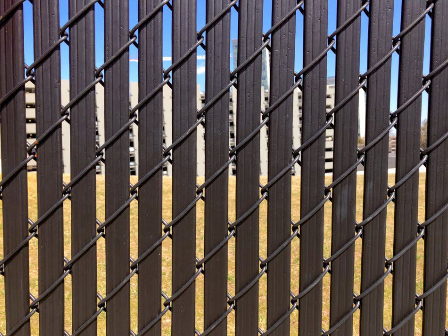 A black metal fence with vertical bars and chain links, with a yellow structure blurred in the background.