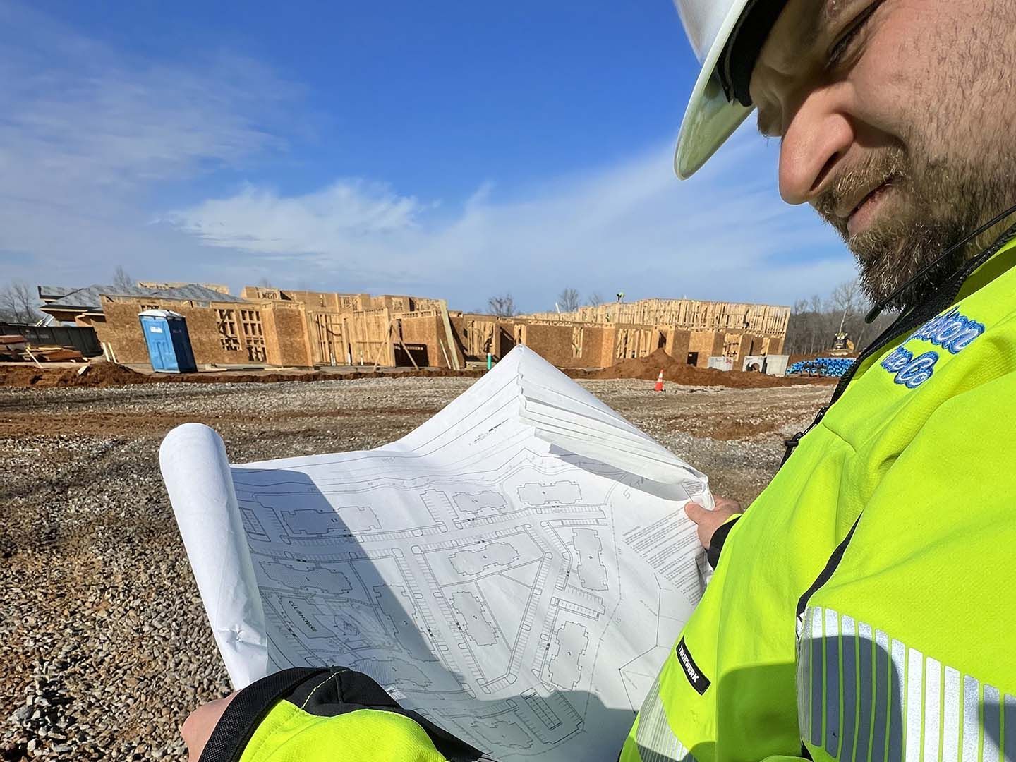 Construction worker in neon vest studying blueprints at a building site under a blue sky