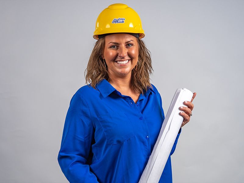 Worker in blue shirt and yellow hard hat holding rolled blueprints and smiling