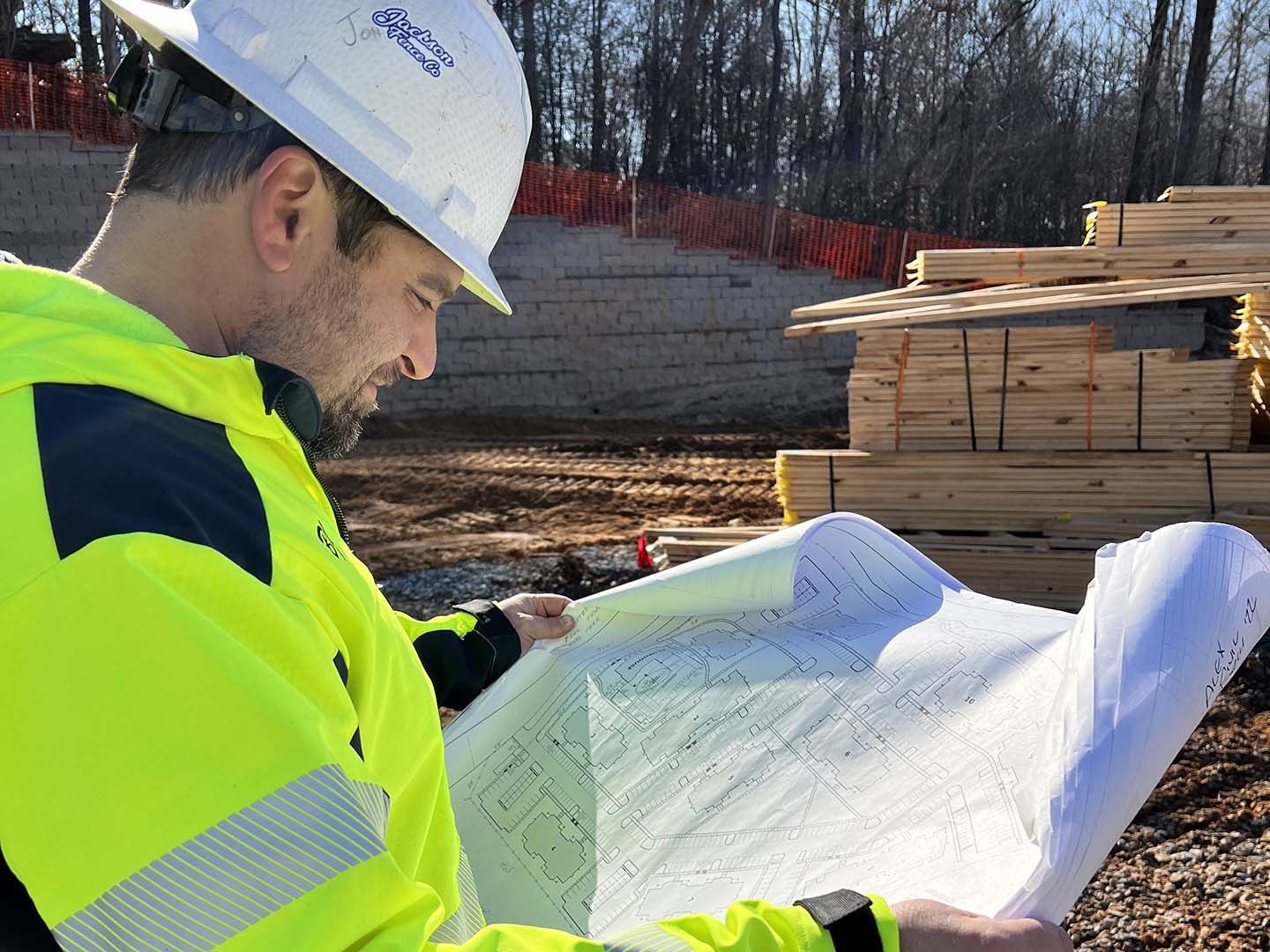 Construction worker in neon jacket and hard hat reviewing blueprints at a building site