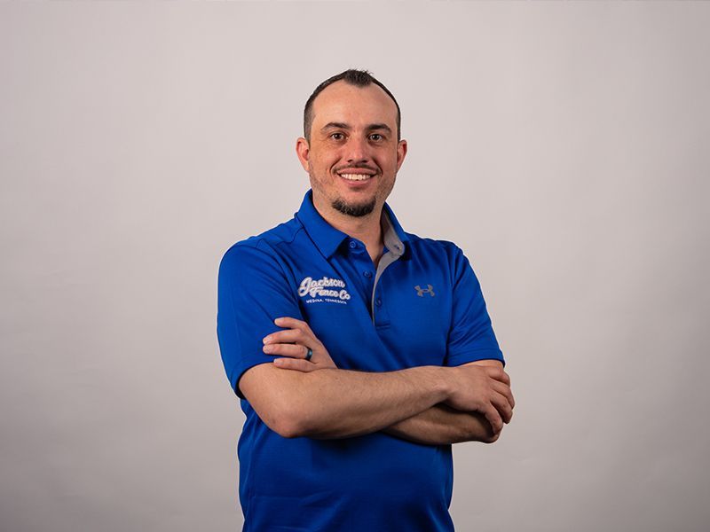 Man in blue polo shirt standing with arms crossed against a light gray background