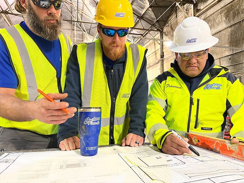 Three construction workers in hard hats reviewing blueprints on a jobsite.
