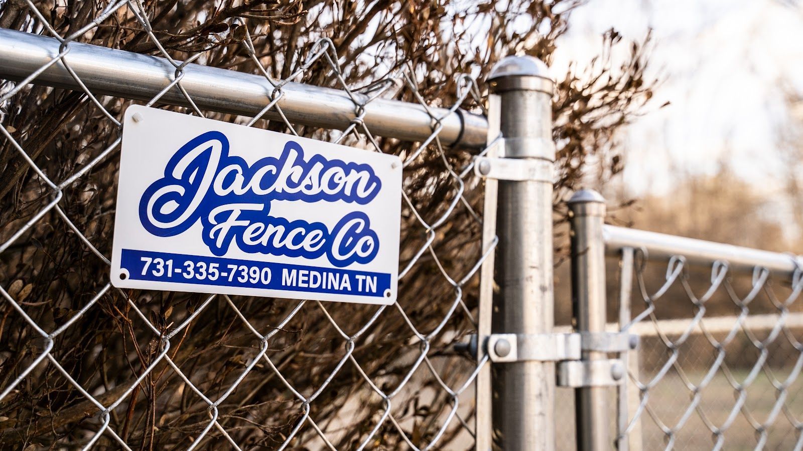 Jackson Fence Co. sign on chain-link fence gate, with phone number and Medina, TN.