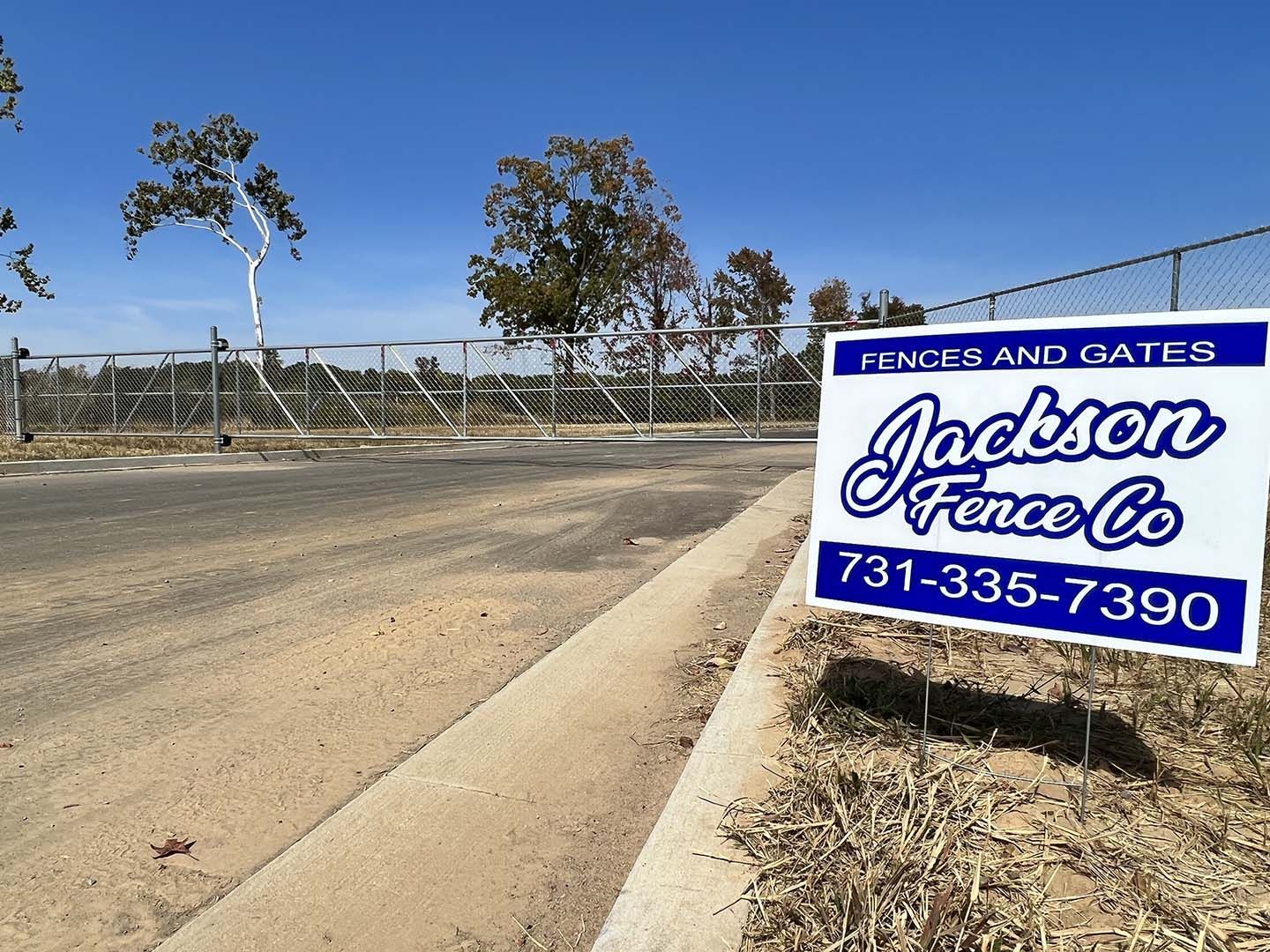 Jackson Fence Co. sign by a dusty roadside and chain-link fence under a clear blue sky