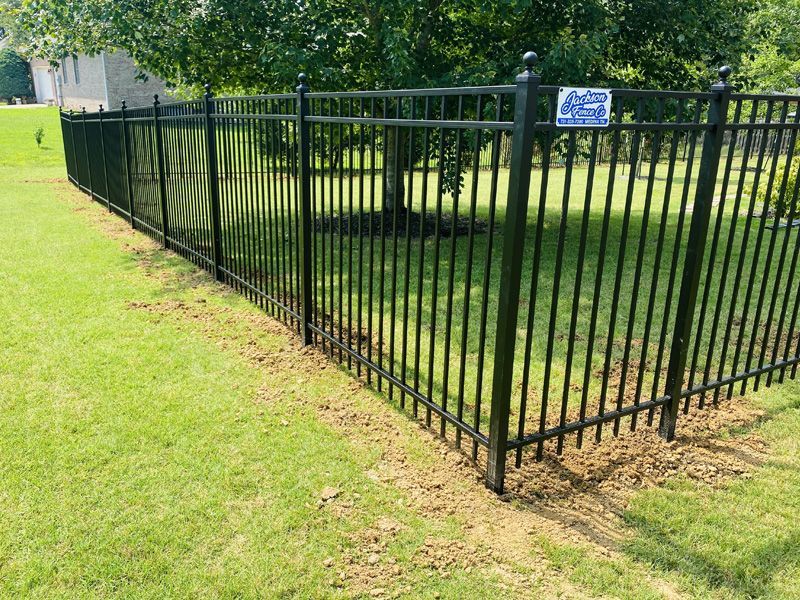 Black metal fence enclosing a grassy yard with trees and a small sign at the corner
