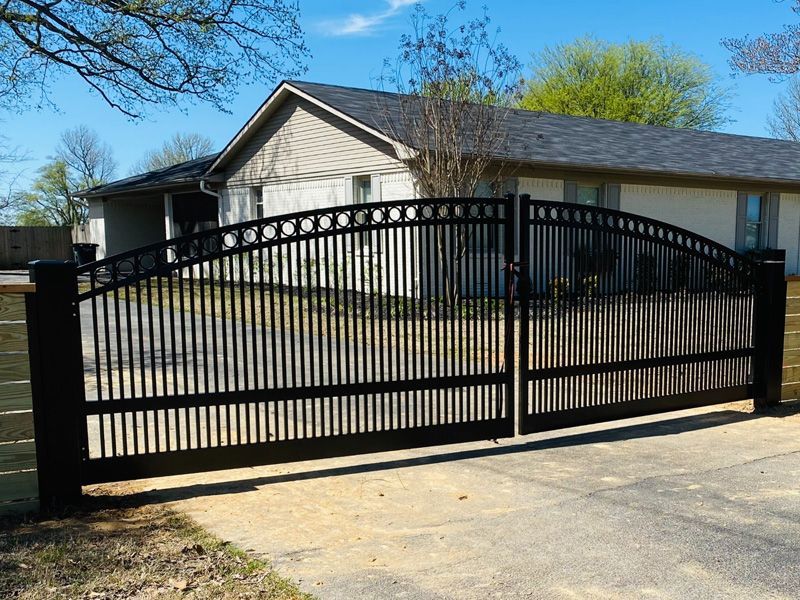 Black metal sliding gate in front of a beige house and driveway, viewed from the street