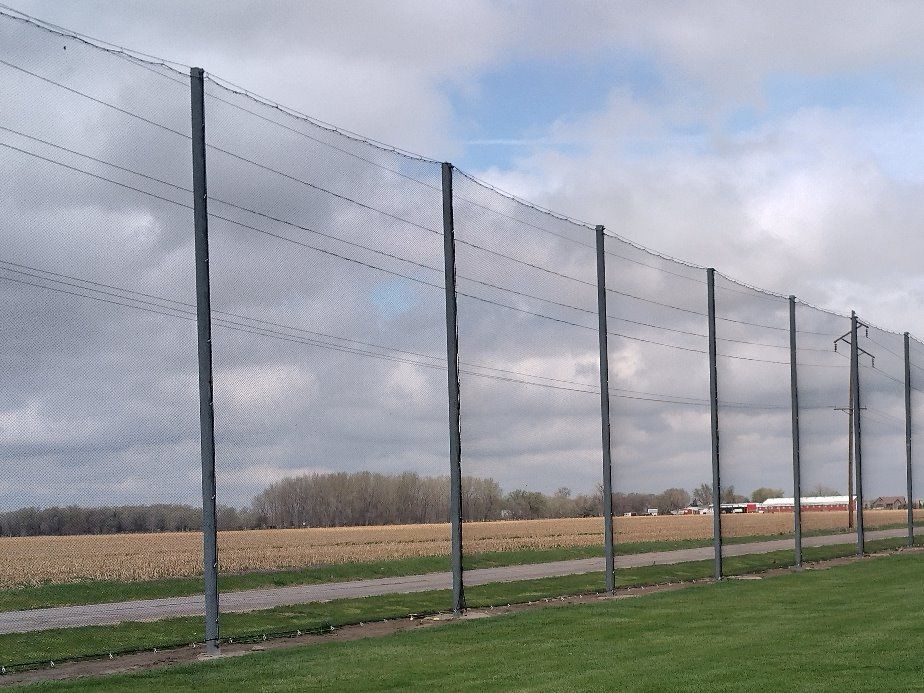 Tall wire fence along a rural field under a cloudy sky