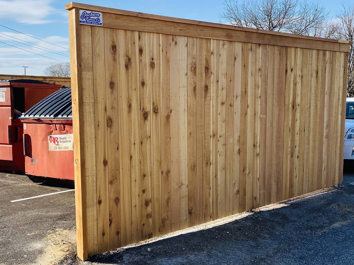 Wooden privacy fence panel beside a red dumpster in a parking lot