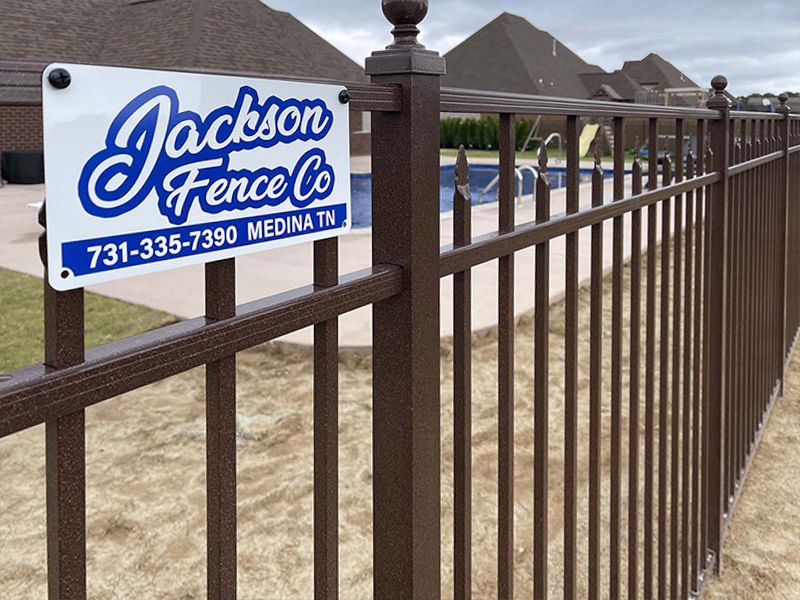 Jackson Fence Co. sign on a brown metal fence near a residential pool area