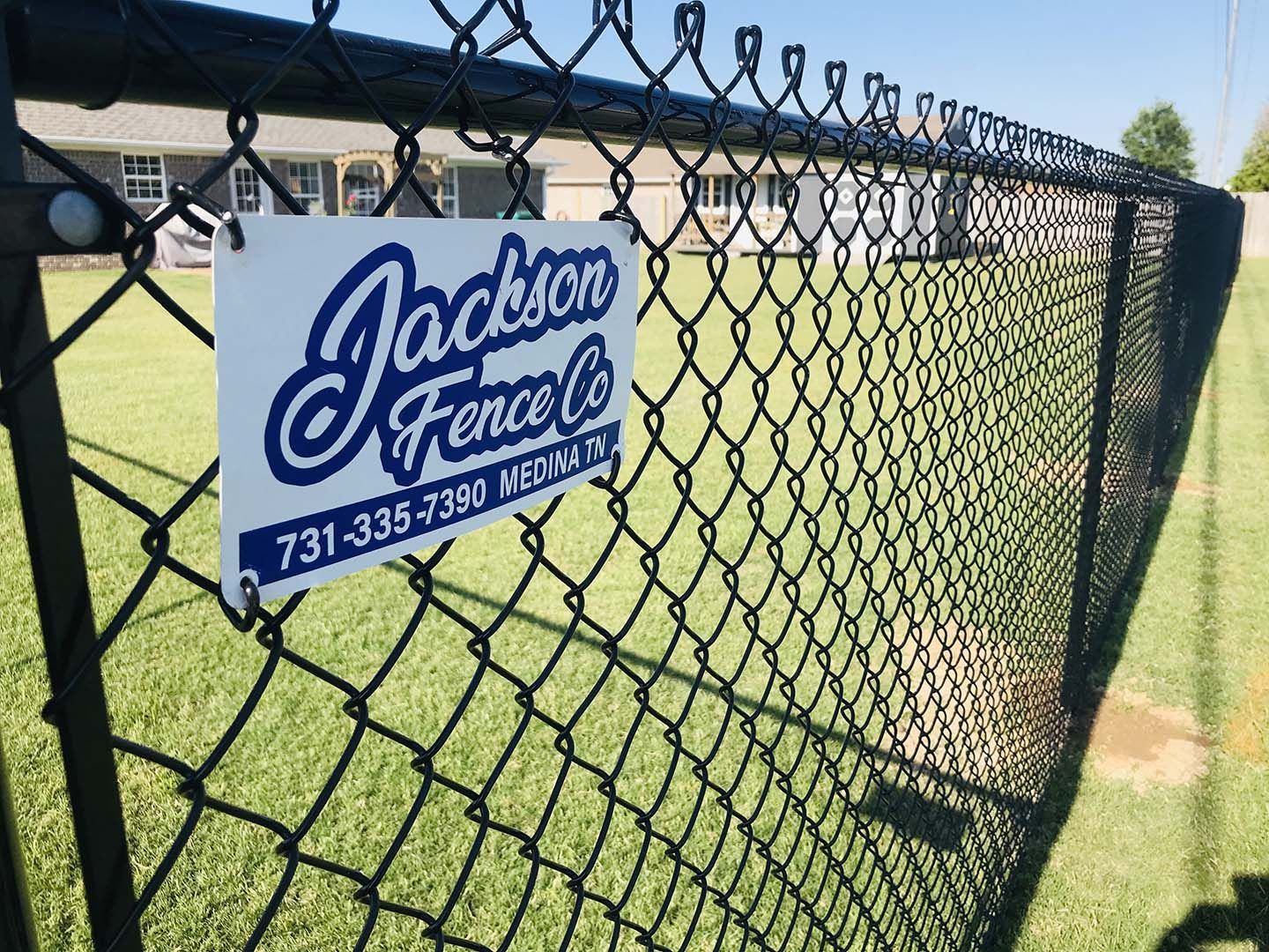 Jackon Fence Co. sign on a chain-link fence beside a grassy field