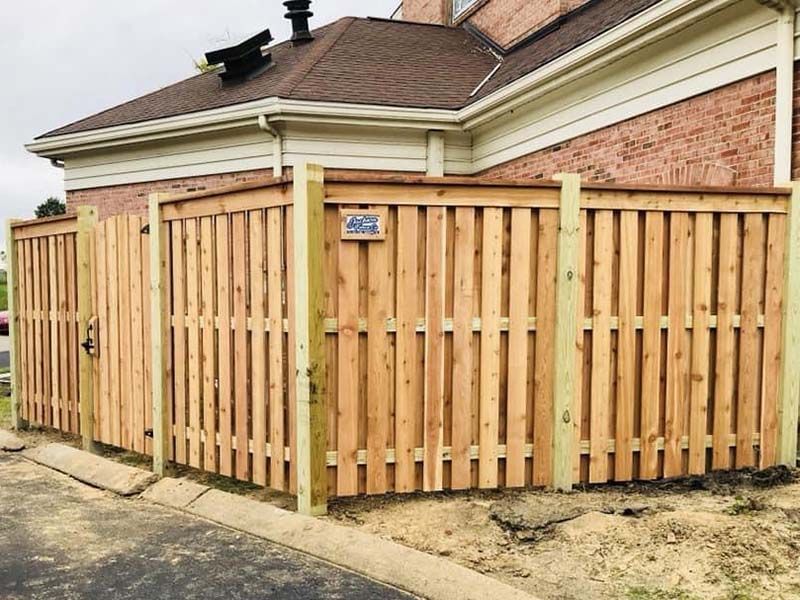 Wooden privacy fence enclosing a brick house corner along a driveway