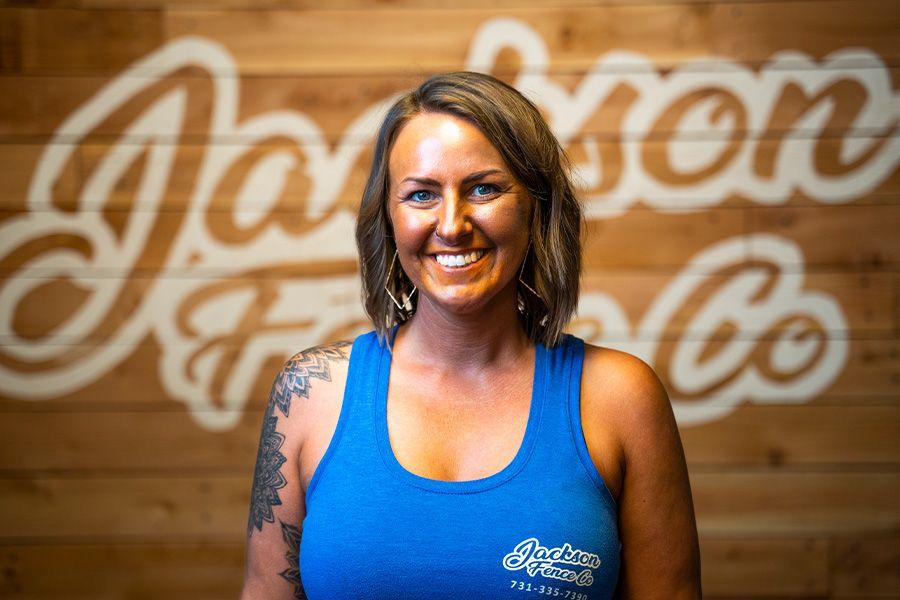 Smiling woman in a blue tank top standing before a wooden wall with a large script logo