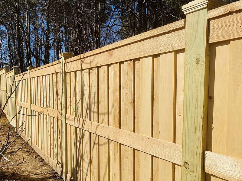 Wooden privacy fence beside a wooded area on a sunny day