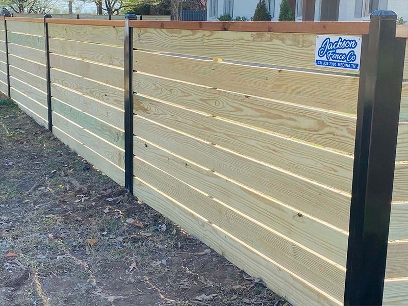Wooden privacy fence with horizontal slats and black posts along a leaf-covered yard