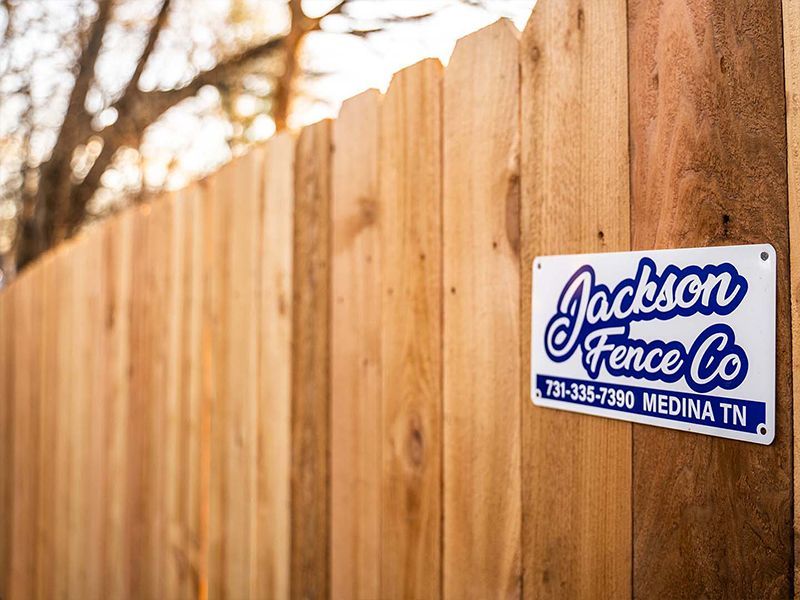 Jackson Fence Co. sign on a wooden fence with trees in the background