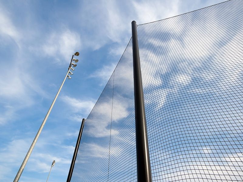 Tall poles and a net fence against a blue sky with clouds
