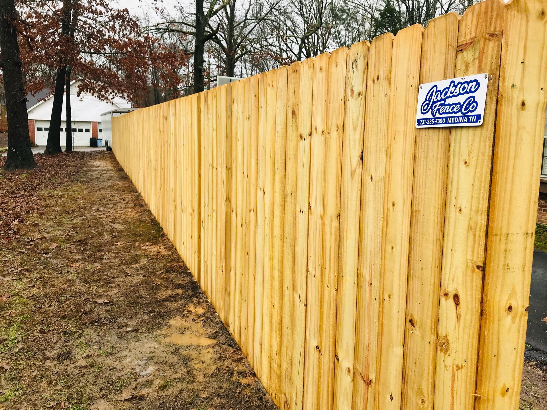 Wooden fence in a yard with a business sign.