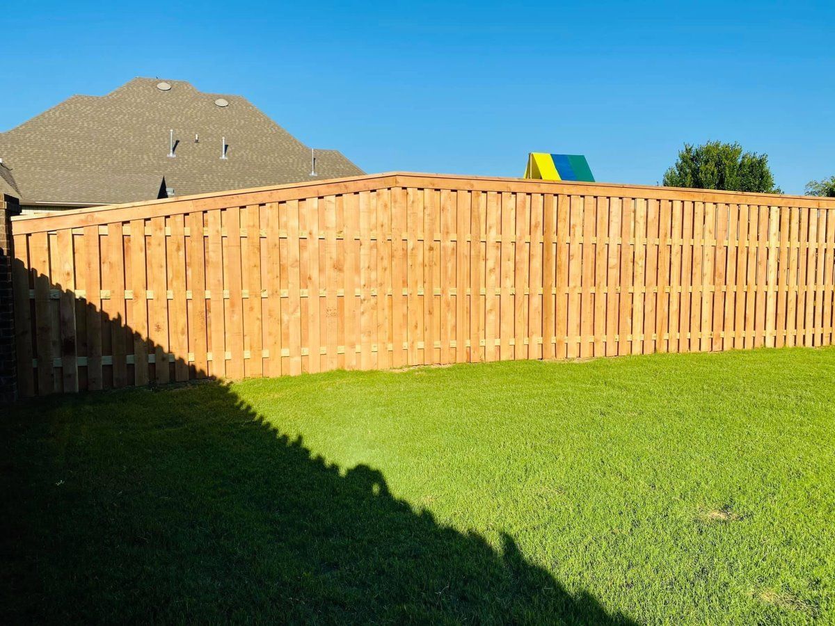 Backyard with wooden fence, green lawn, and house roof under a clear blue sky
