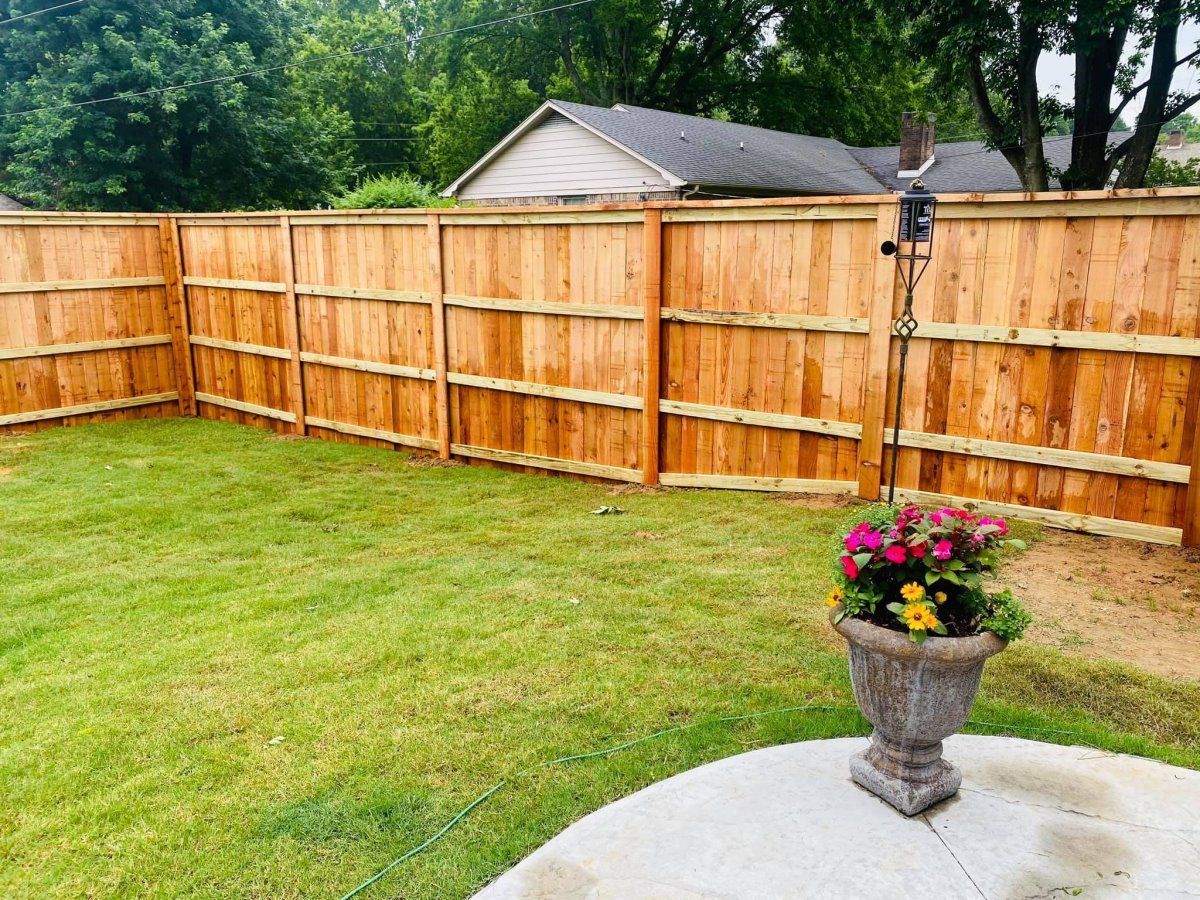 Backyard with wooden fence, green lawn, and potted flowers on a patio[0m
