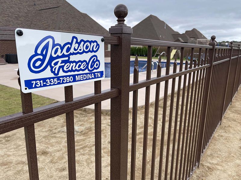 Jackson Fence Co. sign beside a brown metal fence at a home exterior