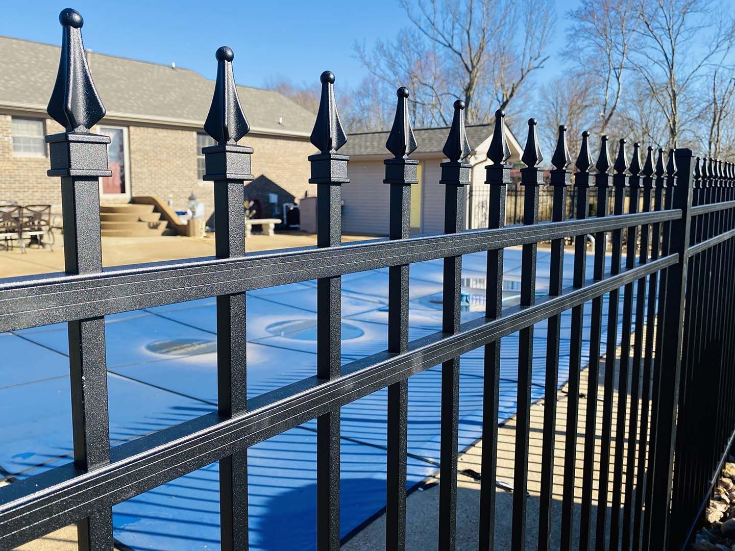 Black metal fence with pointed finials in front of a snowy park and stone steps under a blue sky