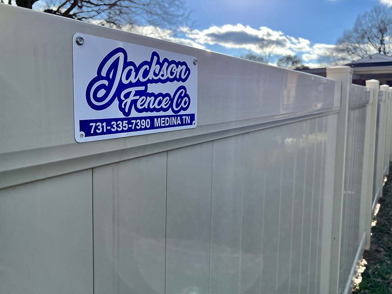White fence with a Jackson Fence Co. sign under a cloudy sky