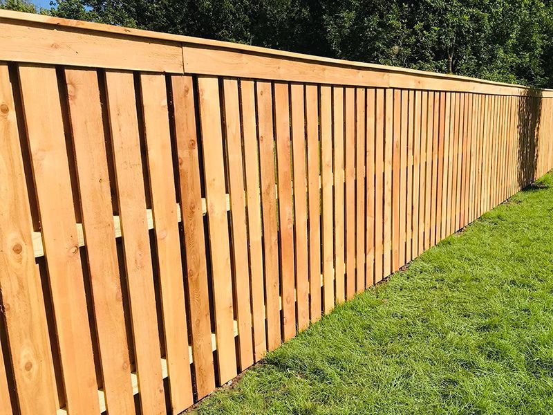 Long wooden fence with vertical slats beside a green lawn in sunlight