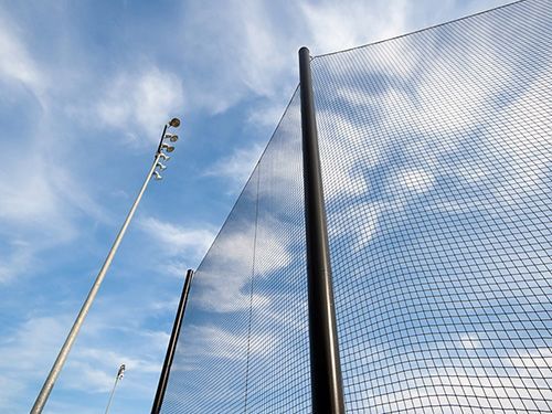 Tall sports net and light poles against a blue sky with scattered clouds