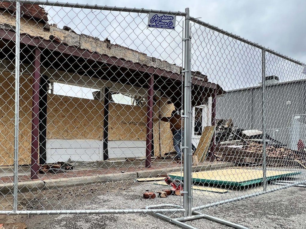 Chain-link fence around a damaged building with debris and construction materials outside.