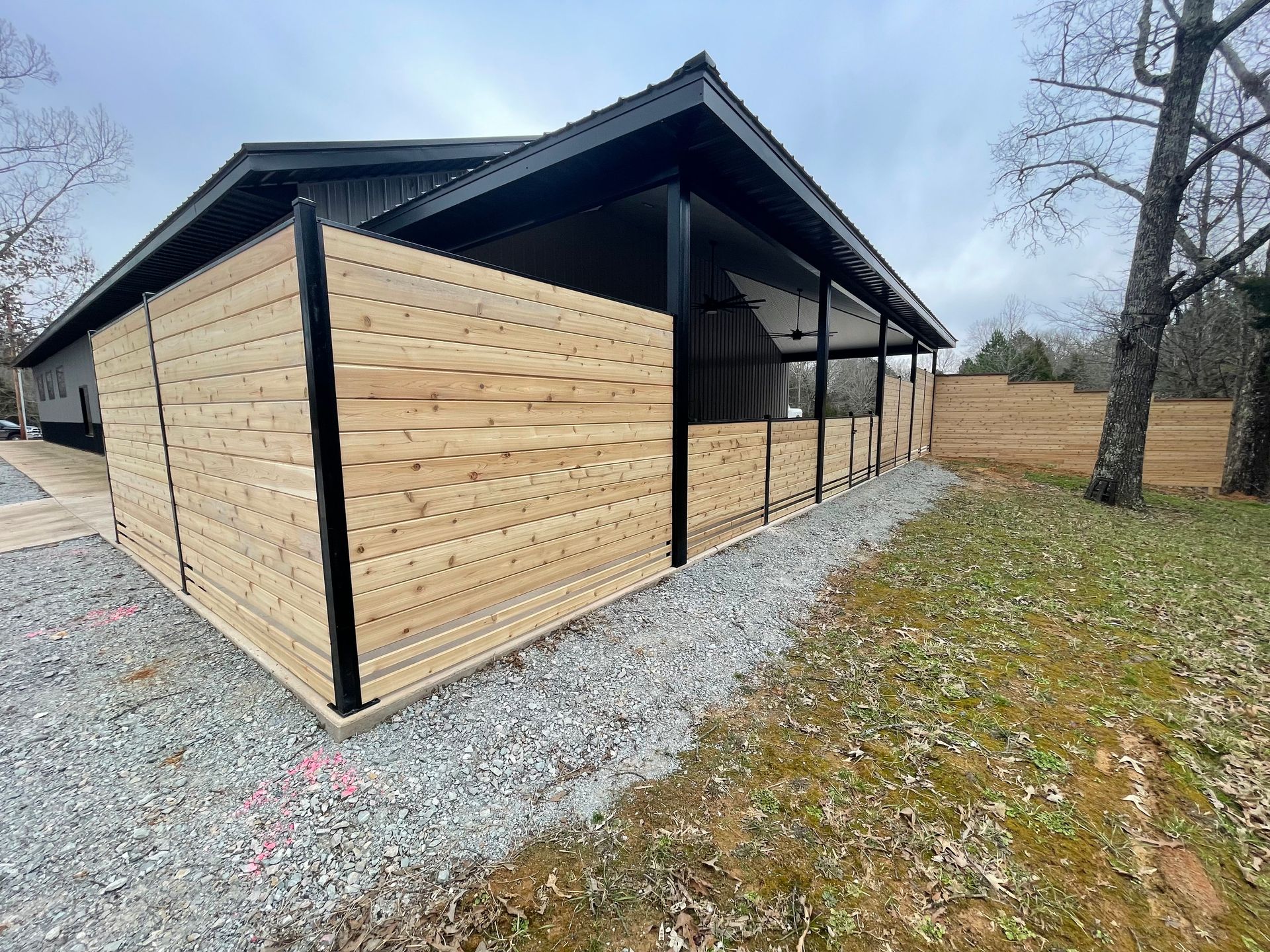 Modern beige-sided barn or shed with black trim on a gravel lot beside a grassy field