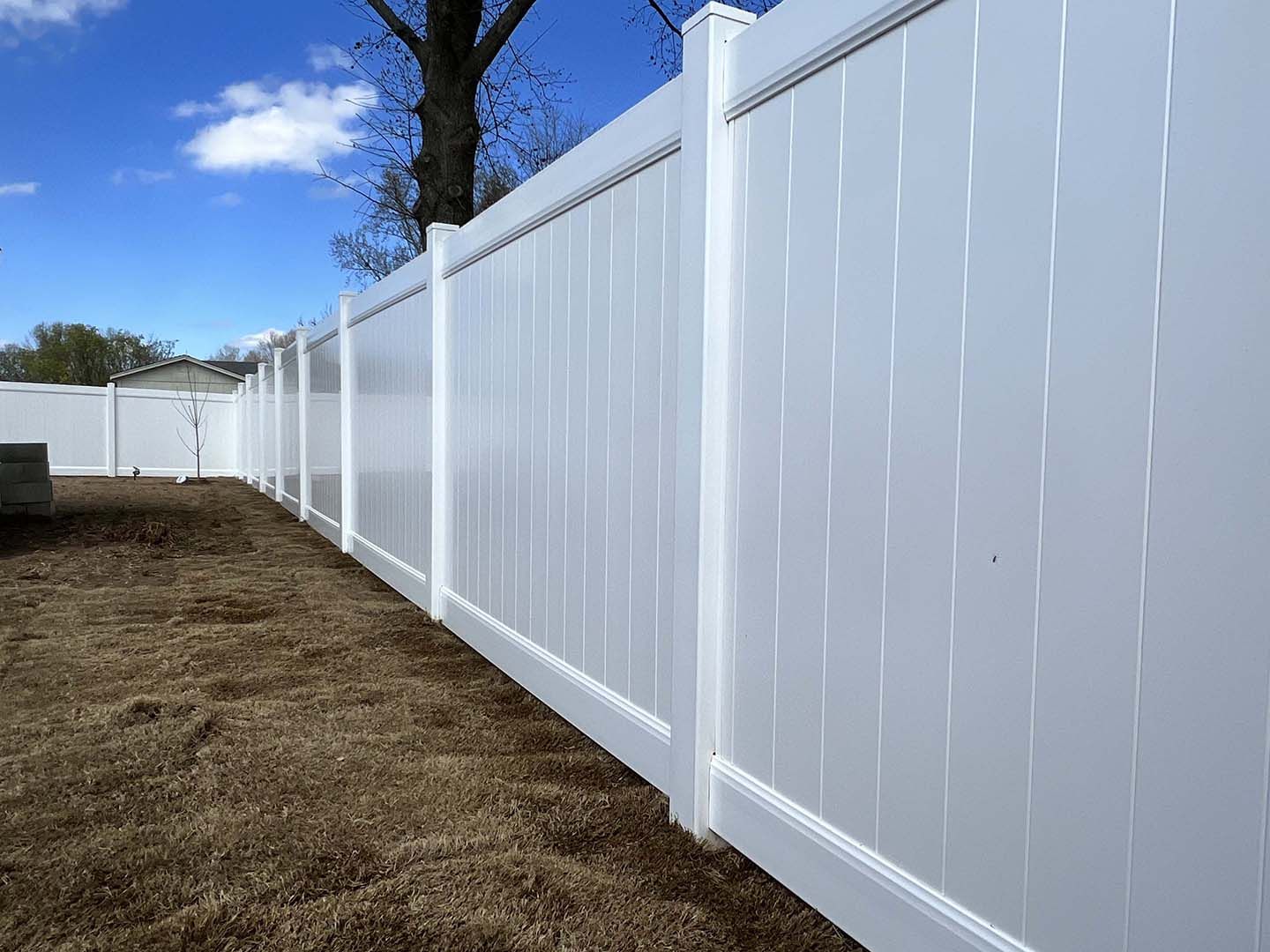 White vinyl fence along a dirt yard under a blue sky, receding into the distance