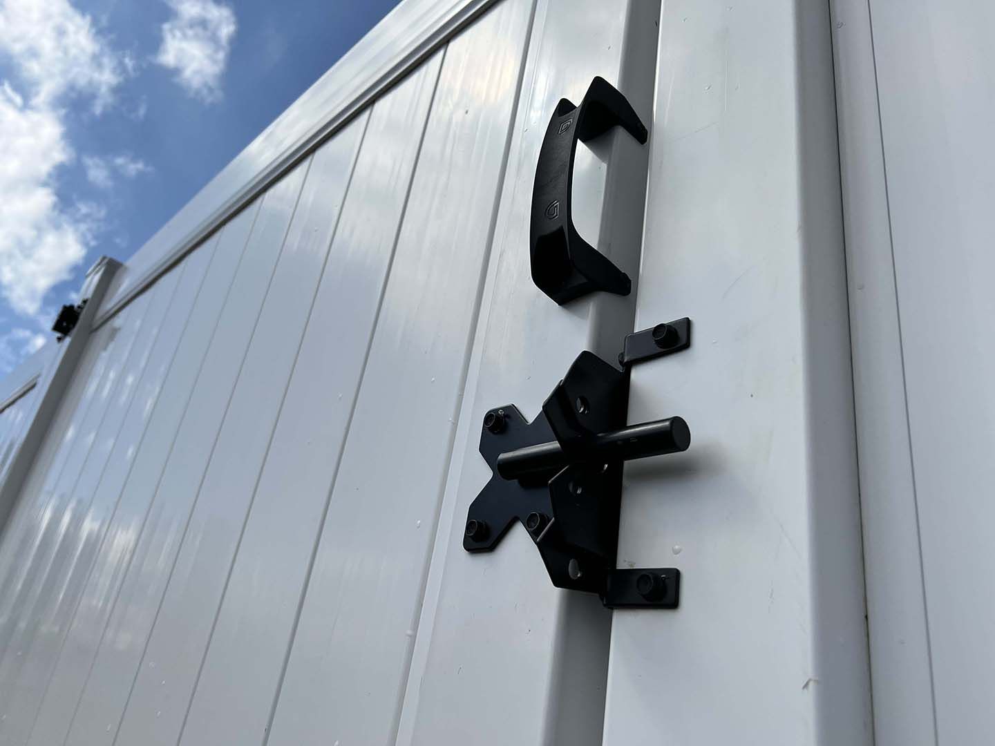 Black latch and handle on a white truck or trailer door against a blue sky.