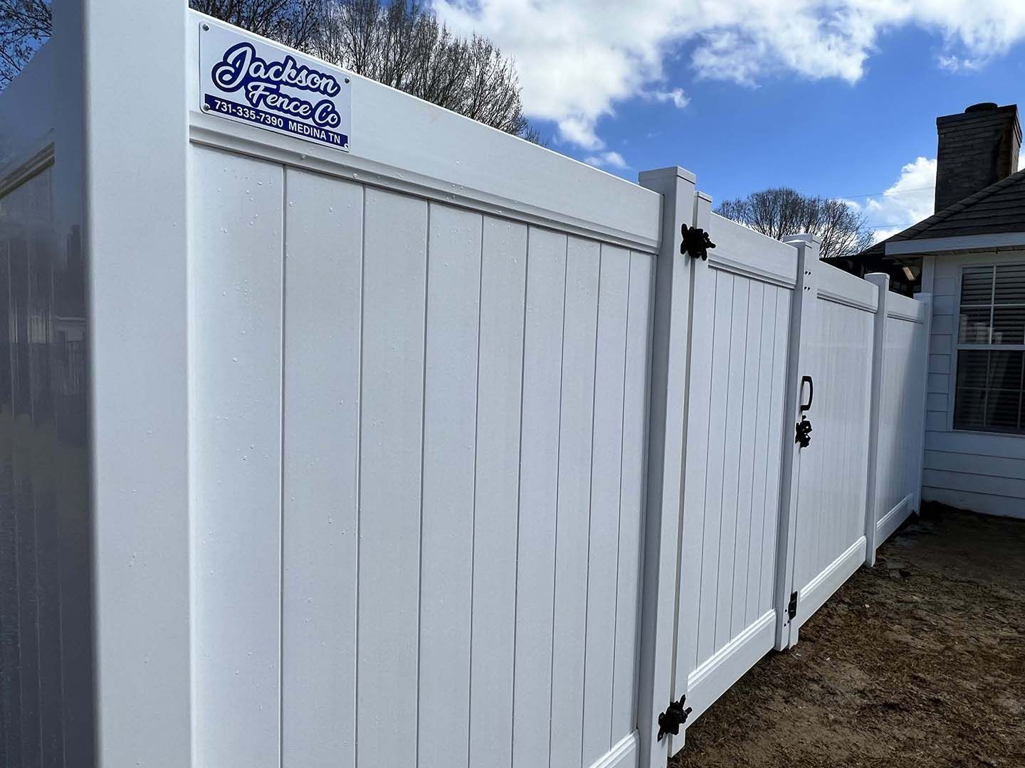 White vinyl privacy fence beside a house with a blue sky overhead