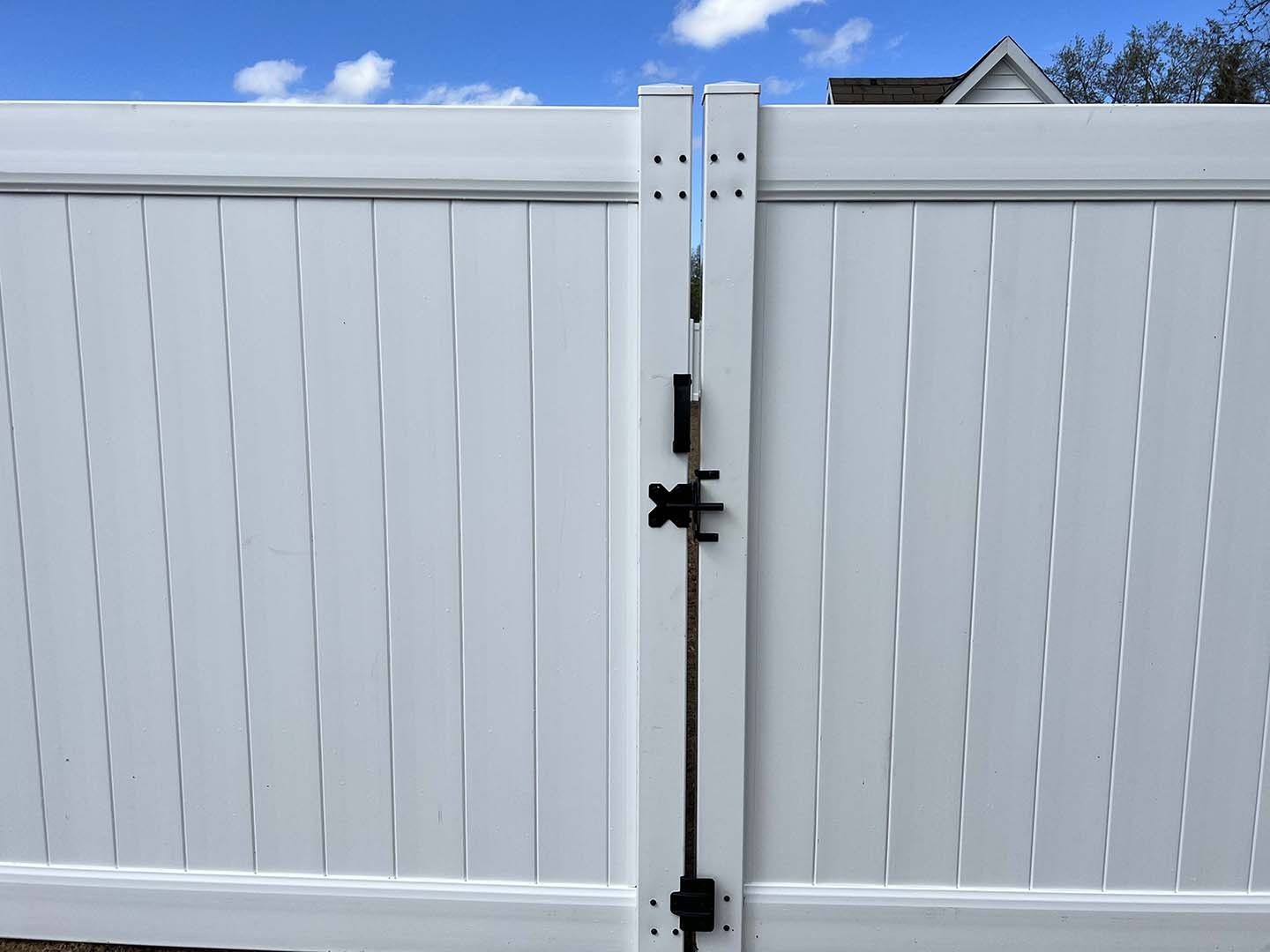White vinyl fence gate with black latch and metal hinges under a blue sky