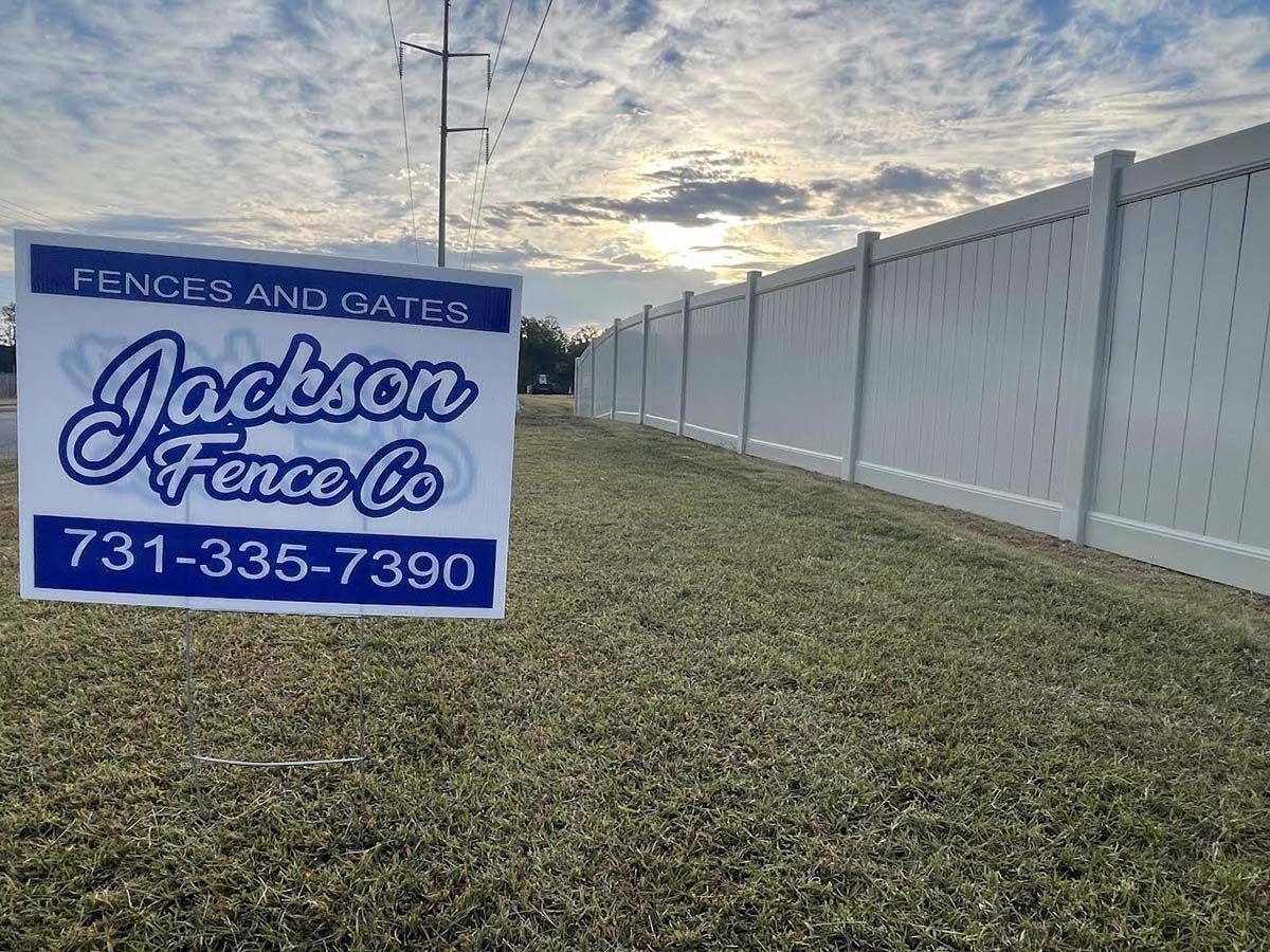 Jackson Fence Co. sign beside a long white privacy fence on a grassy slope.