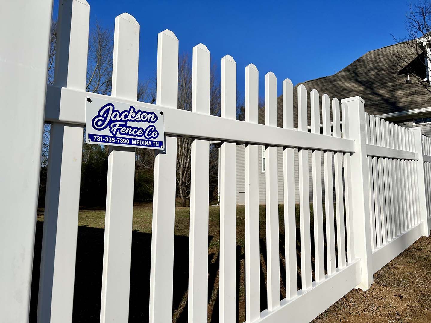 White picket gate with a “Jackson” sign beside a grassy hill under a blue sky