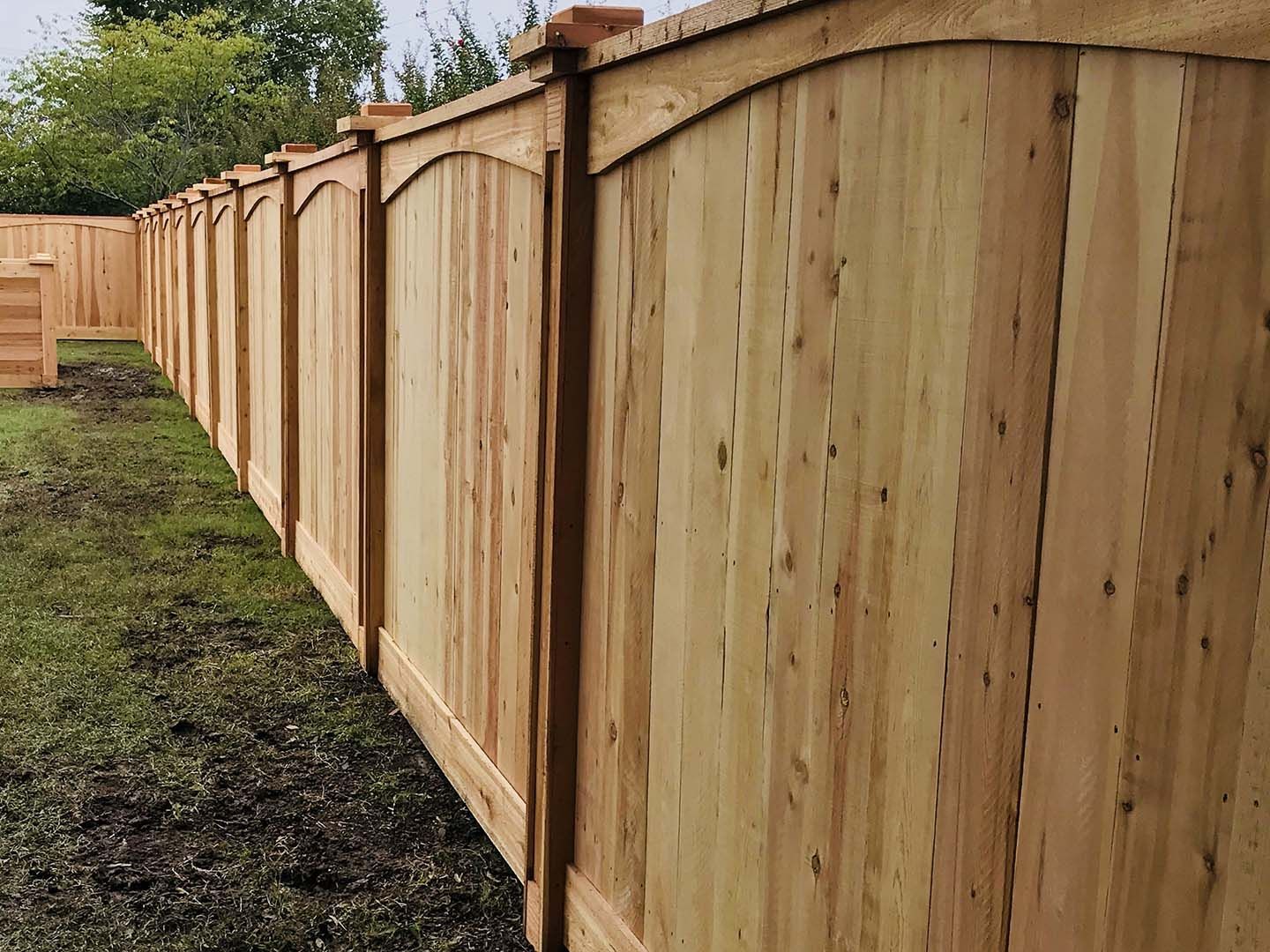 New wooden privacy fence extending along a grassy yard under overcast skies