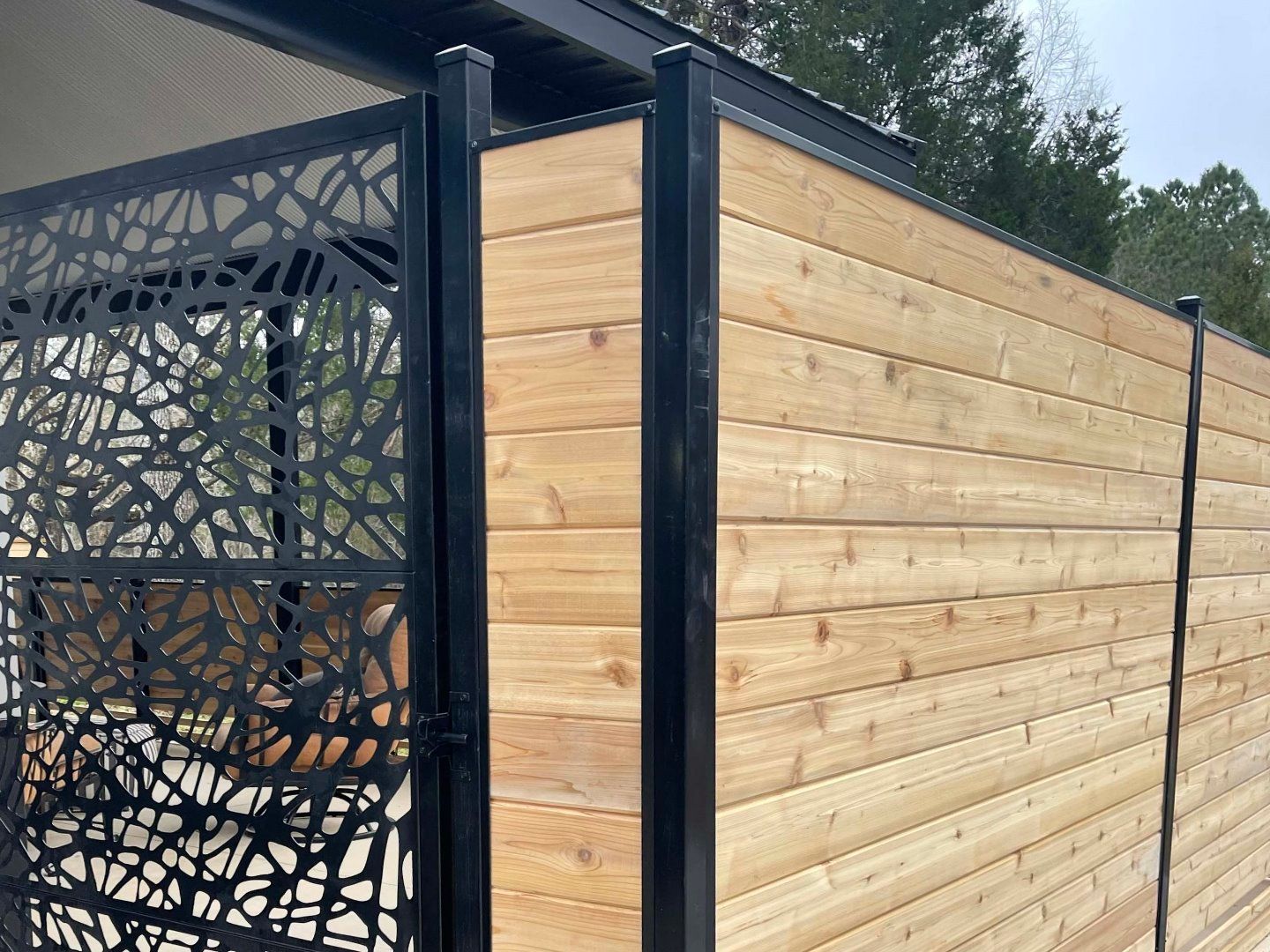 Modern wood-and-black outdoor privacy screen with decorative metal lattice panel.