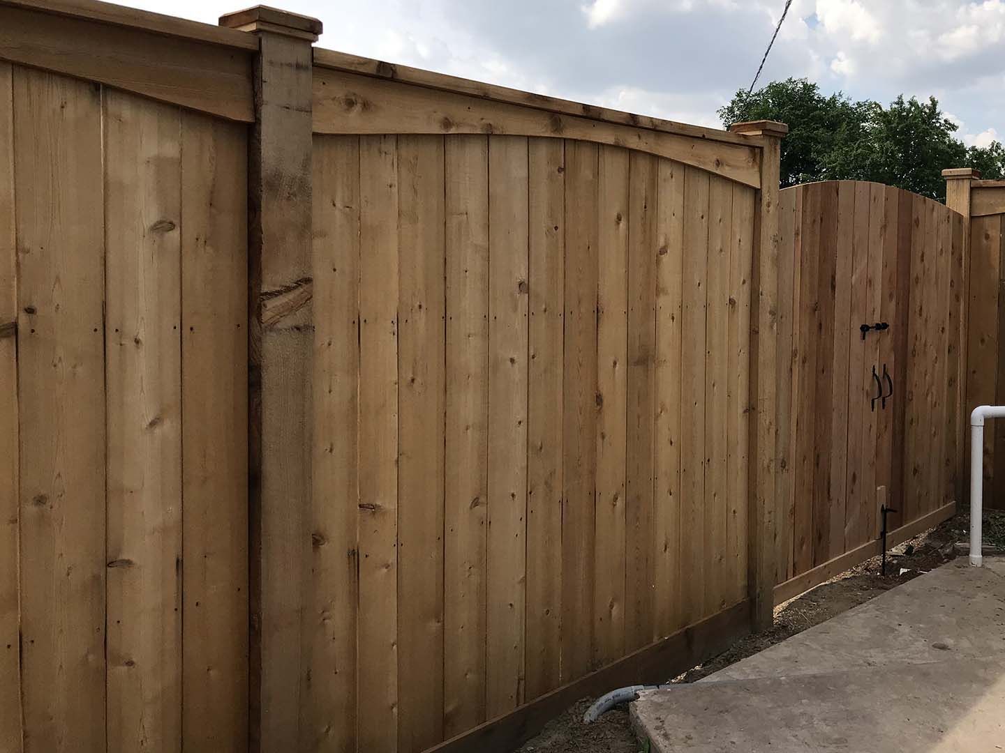 Wooden privacy fence along a concrete driveway under an overcast sky