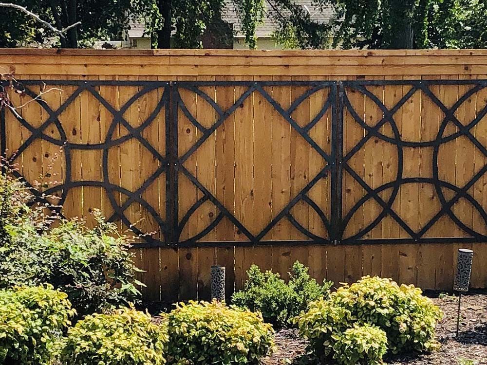 Wooden garden fence with black lattice trim behind shrubs and flowering plants