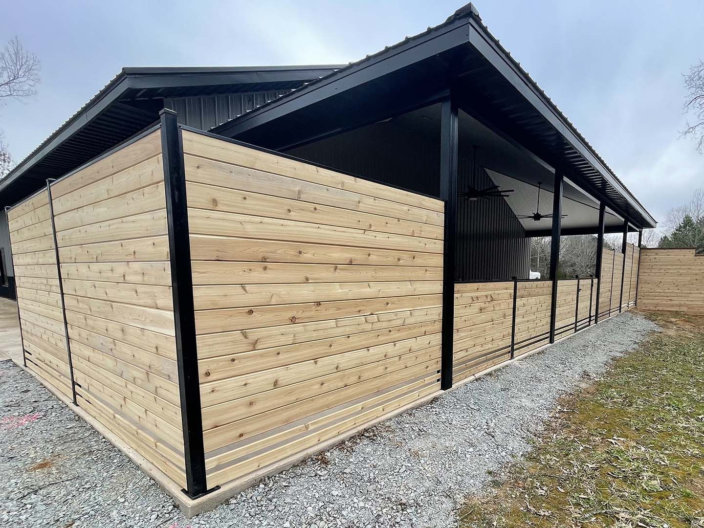 Wood-sided modern barn with black trim and gravel path under overcast sky