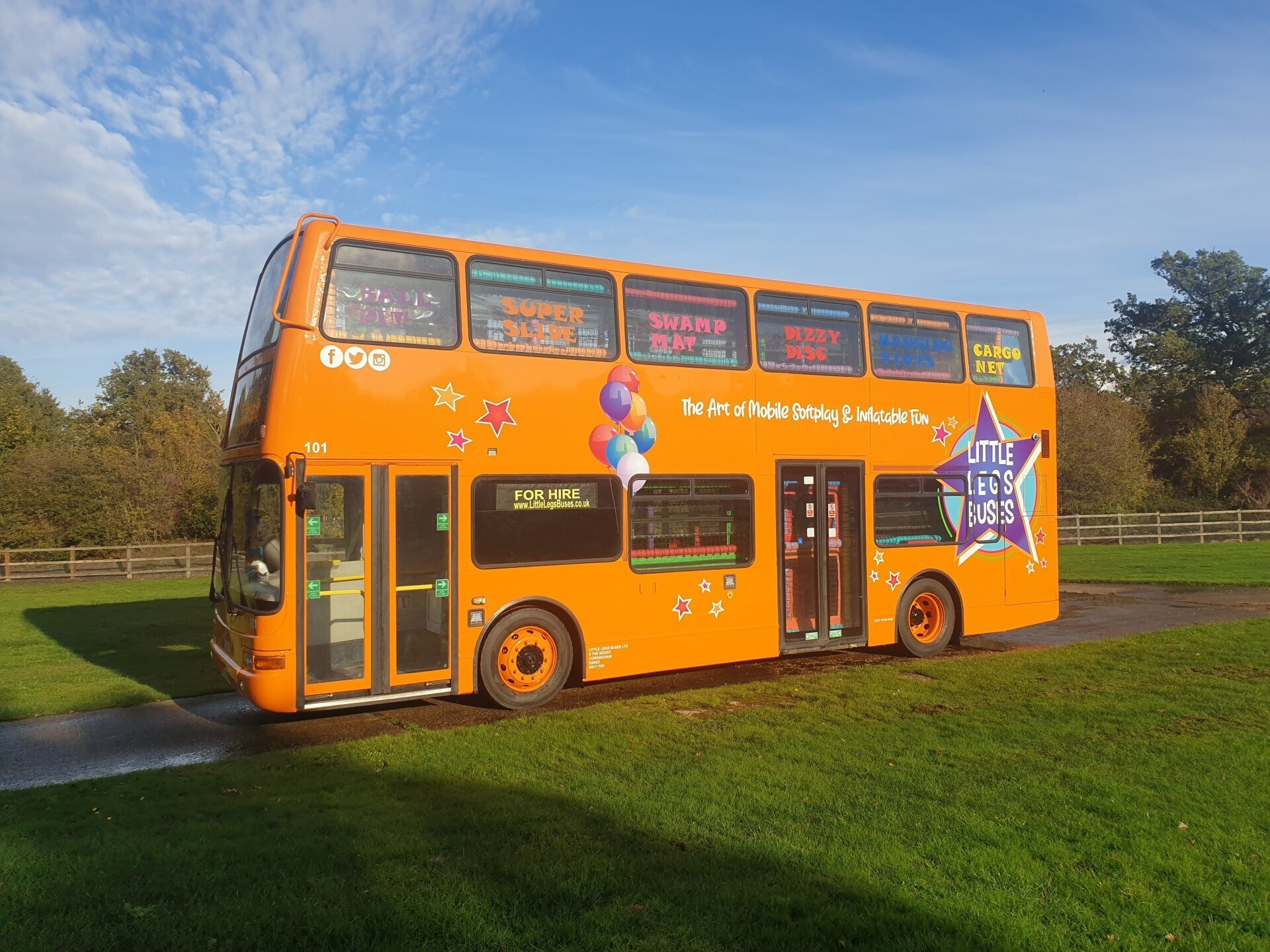 An orange double decker bus is parked in a grassy field.