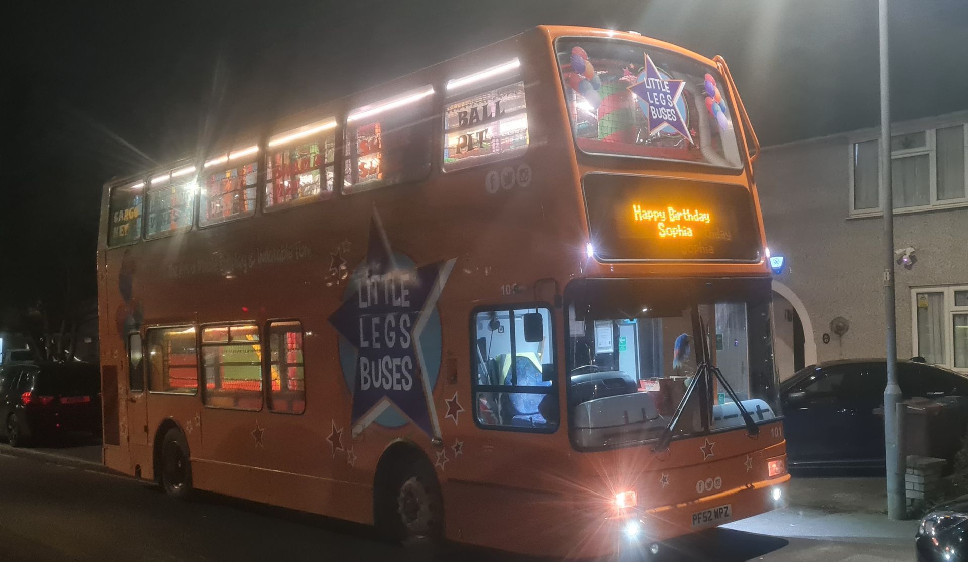 A double decker bus is parked on the side of the road at night.
