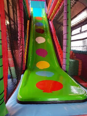 A green slide with polka dots on the floor in a playground.
