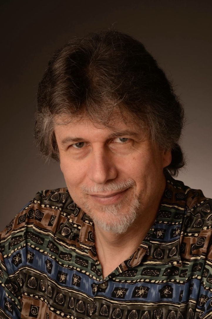 A man with a beard is wearing a colorful shirt and smiling for the camera.