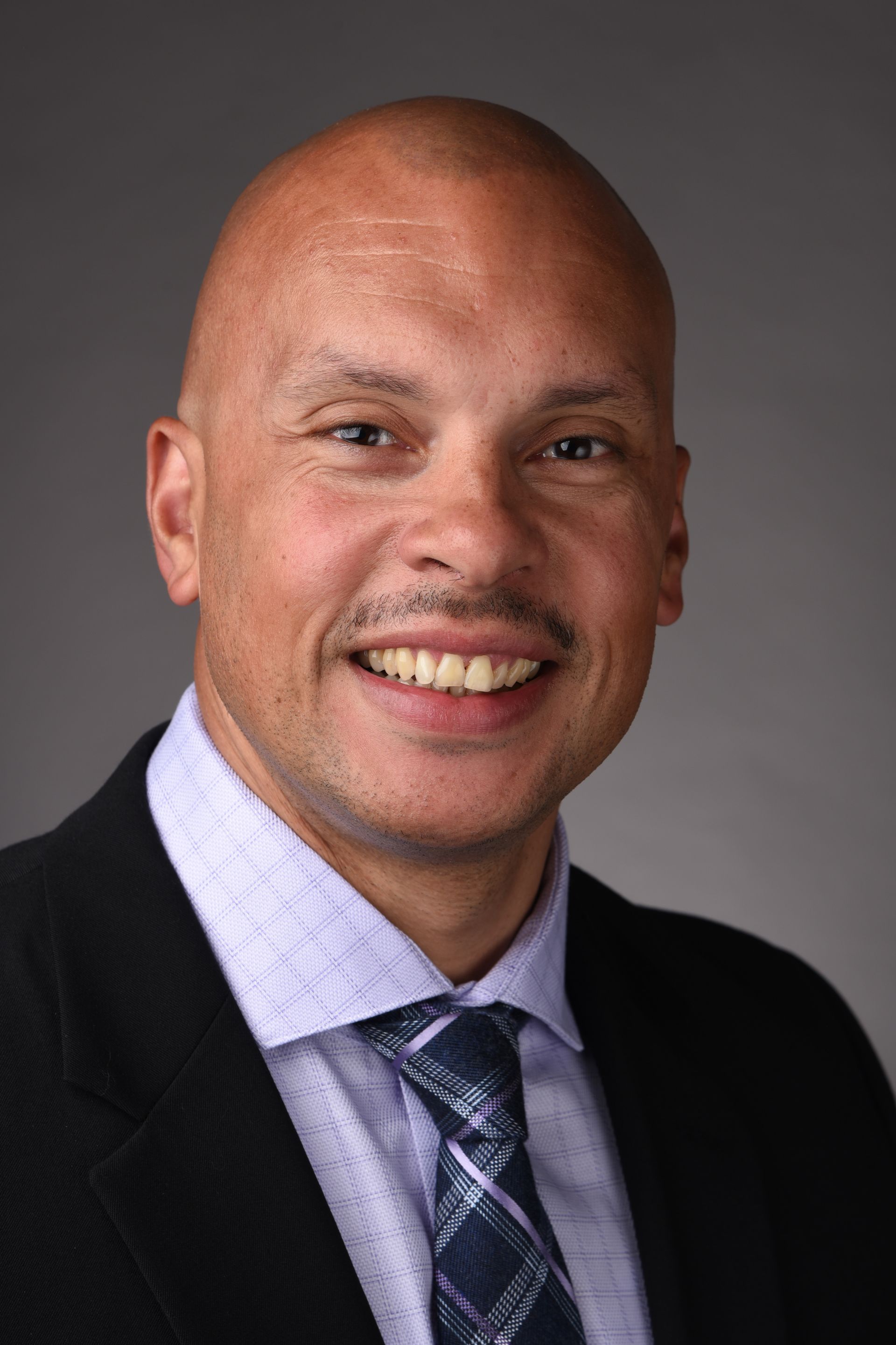 A bald man in a suit and tie is smiling for the camera.
