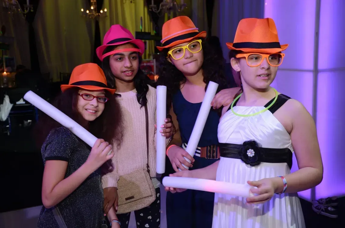 A group of young girls wearing hats and glasses are holding light sticks.