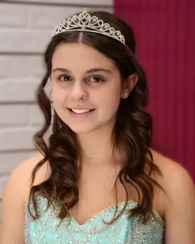 A young girl wearing a tiara and a dress is smiling.