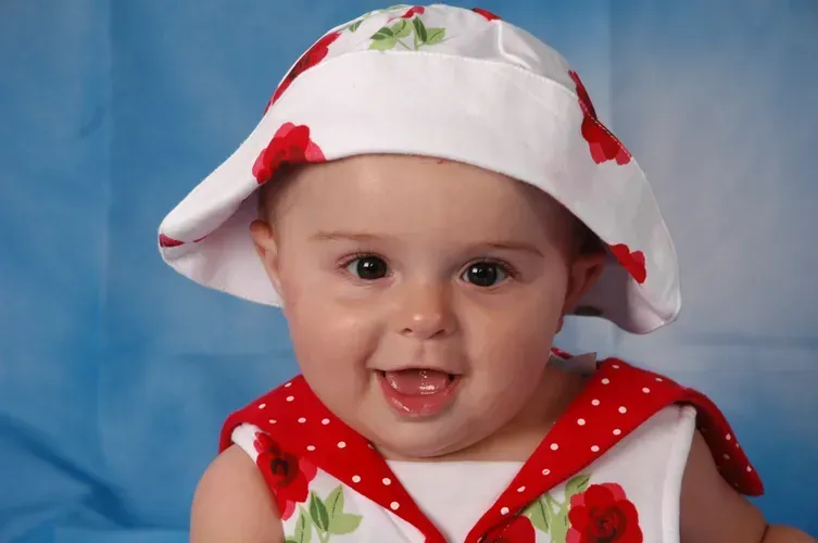 A baby wearing a white hat with red flowers on it
