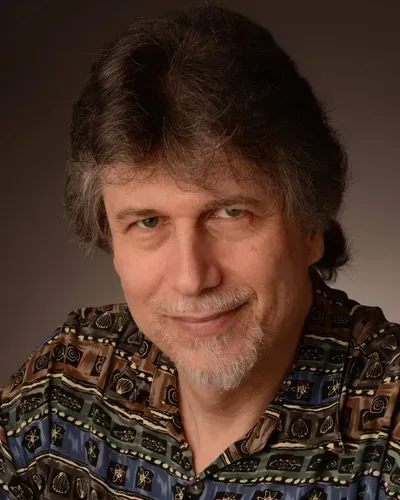 A man with a beard wearing a colorful shirt is smiling for the camera.